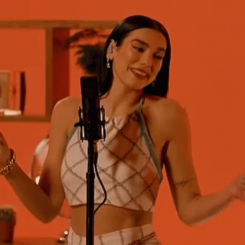 A Woman Is Singing Into A Microphone While Wearing A Crop Top . GIF