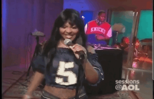 A Woman Is Singing Into A Microphone While Wearing A Number 5 Shirt GIF