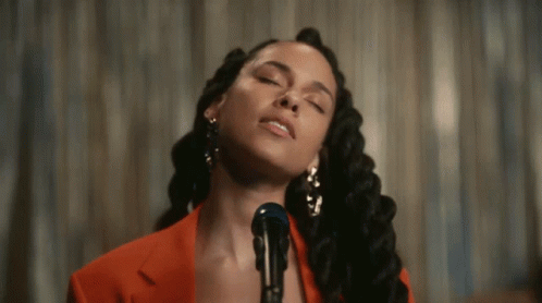 A Woman Is Singing Into A Microphone While Wearing A Red Jacket GIF