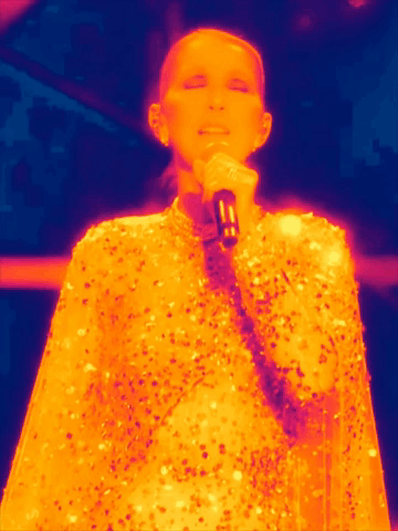 A Woman Is Singing Into A Microphone While Wearing A Sequined Cape GIF