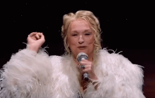 A Woman Is Singing Into A Microphone While Wearing A White Fur Coat . GIF
