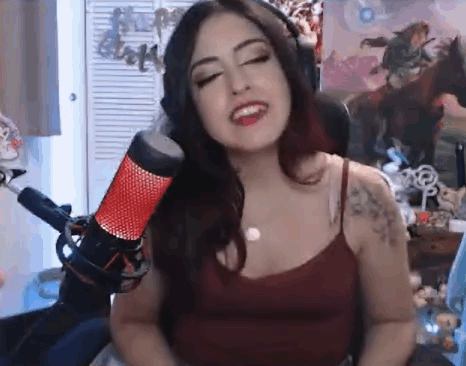 A Woman Is Singing Into A Microphone While Wearing Headphones And A Red Tank Top . GIF