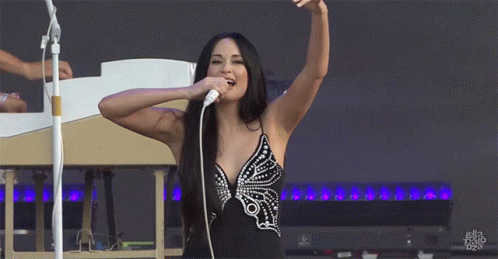 A Woman Is Singing Into A Microphone With Her Arms In The Air And The Word Ella On The Bottom Left GIF