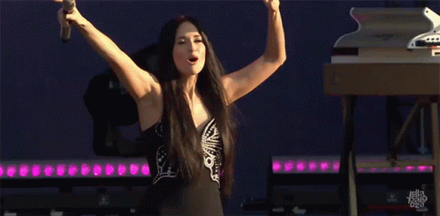 A Woman Is Singing Into A Microphone With Her Arms Outstretched GIF