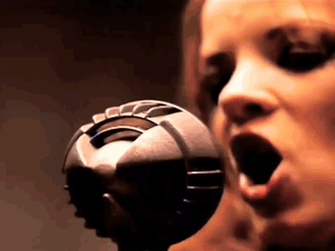 A Woman Is Singing Into A Microphone With Her Mouth Wide Open GIF