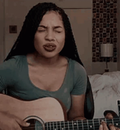 A Woman Is Singing While Playing A Guitar In A Room . GIF