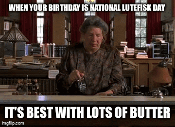 A Woman Is Sitting At A Desk In A Library Holding A Glass Of Butter GIF