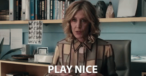 A Woman Is Sitting At A Desk In Front Of A Bookshelf And Saying Play Nice . GIF