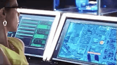 a woman is sitting at a desk in front of two computer monitors .