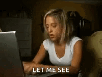 A Woman Is Sitting At A Desk Using A Laptop Computer And Says `` Let Me See '' . GIF