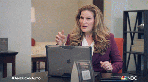 a woman is sitting at a desk with an apple laptop and a sign that says americanauto