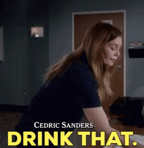 A Woman Is Sitting At A Desk With The Words Drink That Written On The Bottom . GIF