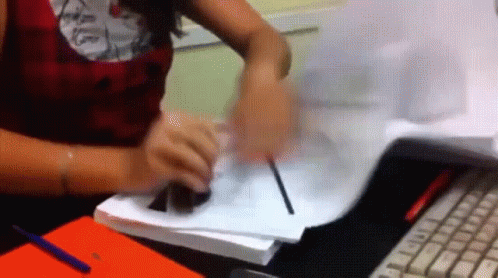A Woman Is Sitting At A Desk Writing On A Piece Of Paper With A Pen GIF