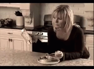A Woman Is Sitting At A Kitchen Counter With A Plate Of Food And A Newspaper . GIF