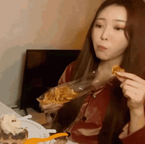 A Woman Is Sitting At A Table Eating A Bag Of Chips GIF