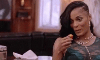 A Woman Is Sitting At A Table Eating A Fried Food . GIF