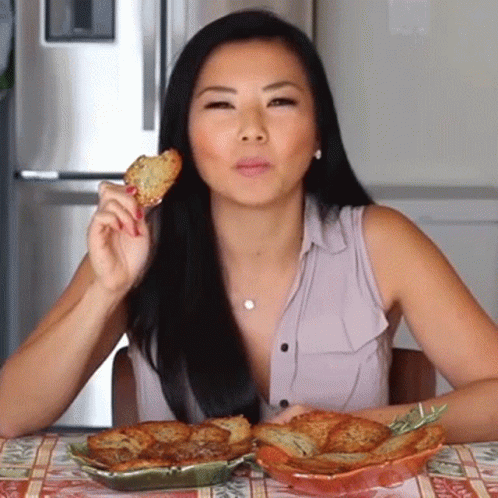 A Woman Is Sitting At A Table Eating A Piece Of Food GIF