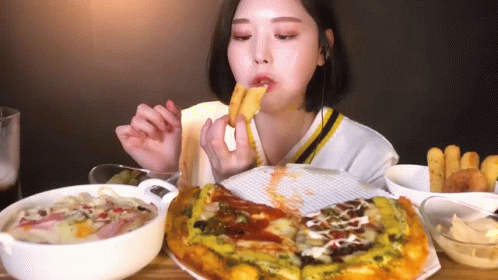 A Woman Is Sitting At A Table Eating A Pizza And French Fries GIF