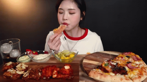A Woman Is Sitting At A Table Eating A Slice Of Pizza . GIF