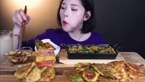 A Woman Is Sitting At A Table Eating Food From A Pan GIF