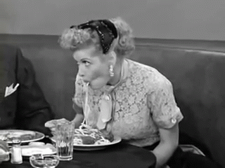 A Woman Is Sitting At A Table Eating Spaghetti With A Spoon GIF