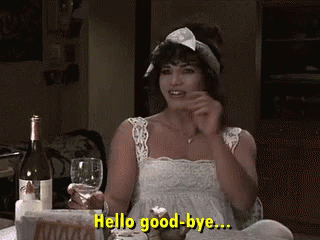 A Woman Is Sitting At A Table Holding A Glass Of Wine And Saying Hello Good-Bye .. GIF