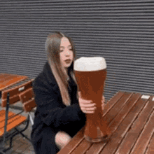 A Woman Is Sitting At A Table Holding A Large Beer Glass . GIF
