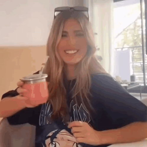A Woman Is Sitting At A Table Holding A Pink Cup . GIF