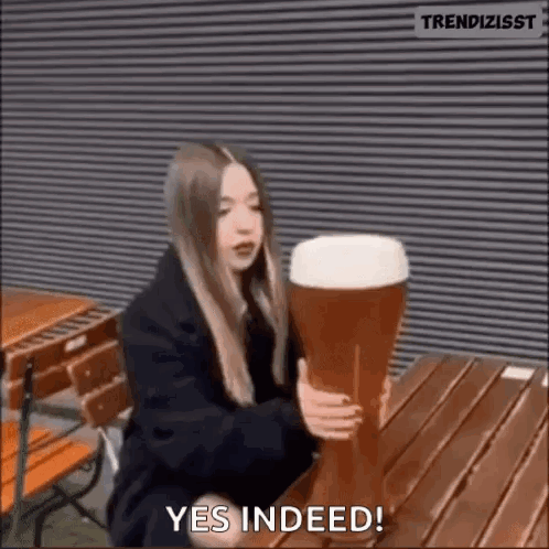 A Woman Is Sitting At A Table Holding A Very Large Glass Of Beer . GIF