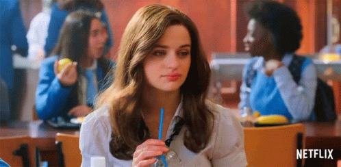 A Woman Is Sitting At A Table In A Cafeteria Drinking Through A Blue Straw . GIF