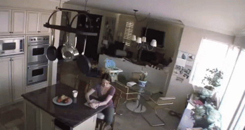 A Woman Is Sitting At A Table In A Kitchen Reading A Book GIF