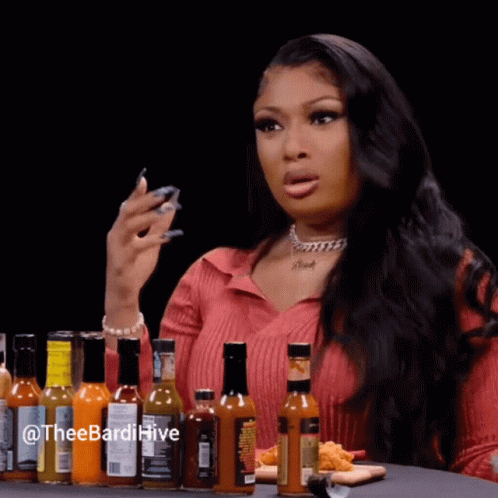 A Woman Is Sitting At A Table Surrounded By Bottles Of Hot Sauce And A Plate Of Food . GIF