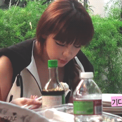 A Woman Is Sitting At A Table With A Bottle Of Water And A Sign That Says ' Gd ' On It GIF