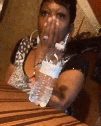 A Woman Is Sitting At A Table With A Bottle Of Water In Her Hand GIF