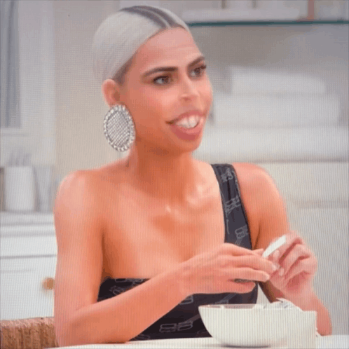 A Woman Is Sitting At A Table With A Bowl Of Cereal And A Spoon GIF