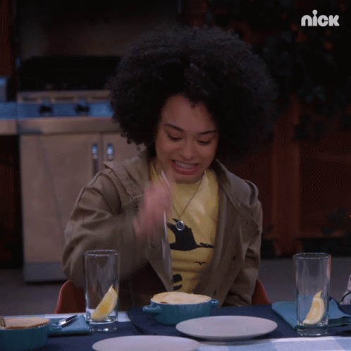 A Woman Is Sitting At A Table With A Bowl Of Food And A Nick Logo On The Bottom GIF