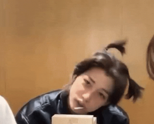 A Woman Is Sitting At A Table With A Box Of Food In Her Hand And Her Hair In A Ponytail . GIF