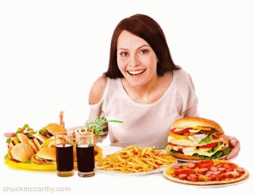 A Woman Is Sitting At A Table With A Bunch Of Food Including A Hamburger French Fries And A Pizza GIF
