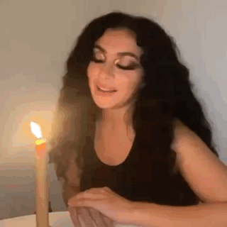 A Woman Is Sitting At A Table With A Candle In Front Of Her . GIF