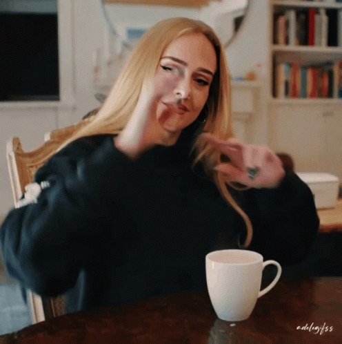 A Woman Is Sitting At A Table With A Cup Of Coffee And The Name Adelaide Is On The Bottom GIF
