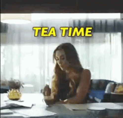 A Woman Is Sitting At A Table With A Cup Of Tea In Her Hand . GIF