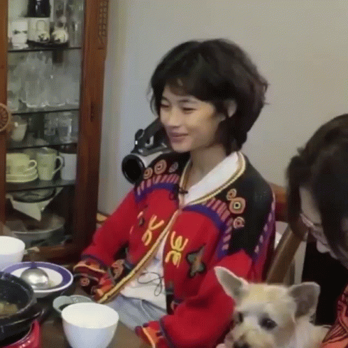 A Woman Is Sitting At A Table With A Dog And Two Women . GIF