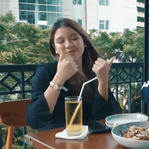 A Woman Is Sitting At A Table With A Glass Of Beer And A Straw . GIF