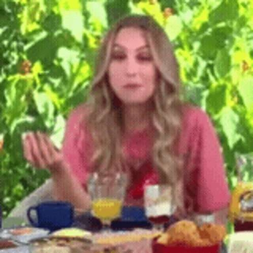 A Woman Is Sitting At A Table With A Glass Of Orange Juice And A Plate Of Food . GIF