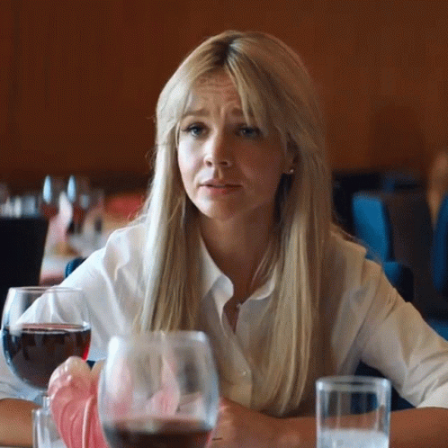 A Woman Is Sitting At A Table With A Glass Of Wine And A Glass Of Water . GIF