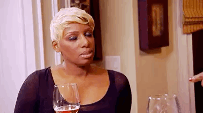 A Woman Is Sitting At A Table With A Glass Of Wine And Making A Funny Face . GIF