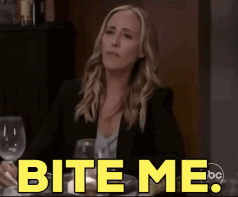 A Woman Is Sitting At A Table With A Glass Of Wine And Says " Bite Me " GIF