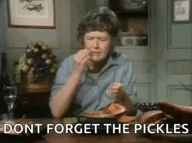 A Woman Is Sitting At A Table With A Plate Of Food And Pickles . GIF