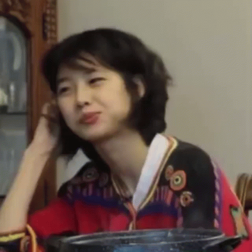 A Woman Is Sitting At A Table With A Pot In Front Of Her And Talking On A Cell Phone . GIF