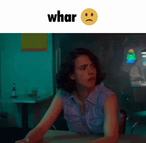 A Woman Is Sitting At A Table With A Sad Face And The Word Whar Behind Her GIF